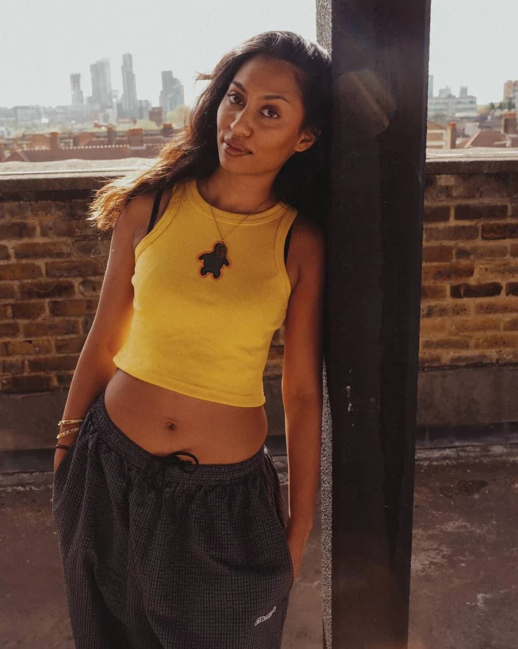 Model leaning by a rooftop pillar in the yellow Art Beyond The Shell vest